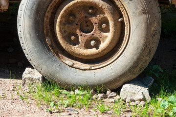 An old car wheel is fixed on both sides with gray mud stones. There is a rusted disc with screws and a worn tire. Background. Texture.