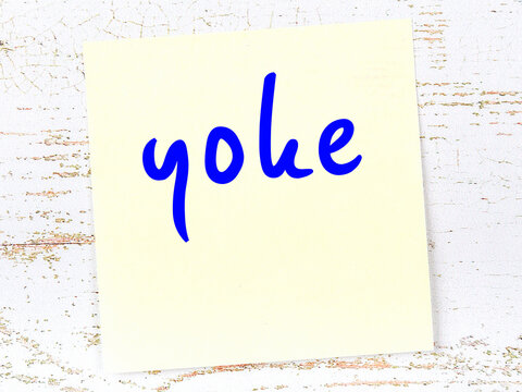 Yellow sticky note on wooden wall with handwritten word yoke