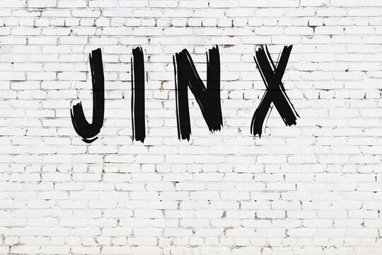 Inscription jinx painted on white brick wall