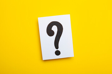 Paper card with question marks on yellow background. Pile of question marks, top view 