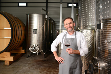 Portrait of a mature man oneologist tasting wine bottle in wine cellar with wooden barrel