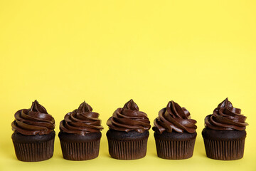Delicious chocolate cupcakes with cream on yellow background. Space for text