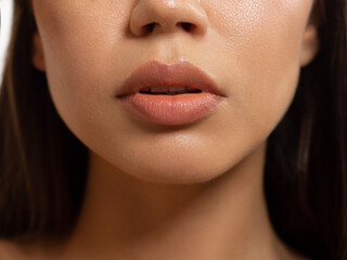 Close-up of woman's lips with fashion natural beige lipstick makeup. Macro sexy pale lipgloss make-up . Gentle pure skin and wavy brunet hair. Cosmetology, Spa, increase in lips - obrazy, fototapety, plakaty