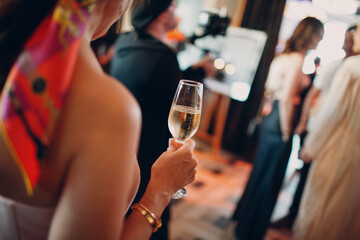 rear view woman holding misted chilled glass of champagne in hand at party.
