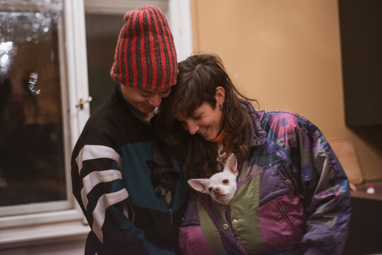 sweet female queer couple cuddle with cute chihuahua dogs in snowcoats