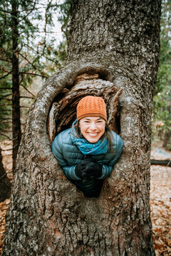 woman wearing hat smiles and laughs inside a large tree knot