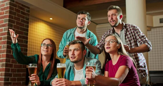Diverse Group of Friends Watches TV in the Sporstbar. Their Team Scores the Goal and Wins. Young People Cheer.