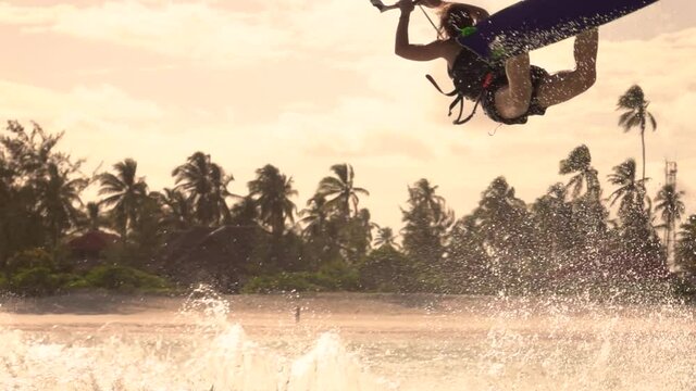 SLOW MOTION, CLOSE UP: Extreme female kitesurfer riding in Zanzibar jumps and does a superman trick on a sunny summer evening. Spectacular shot of a kiteboarder doing a trick in the air while surfing.