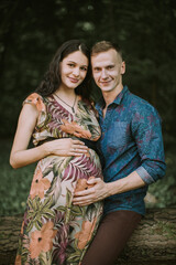 Close up portrait of happy pregnant couple, standing in beautiful summer forest, touching belly and smiling at camera