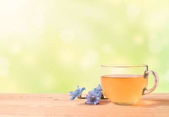 a cup of herbal tea and blue flowers on a wooden table on a green blurred background