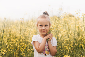 Little pretty girl with canola flowers on the field in summer. Summer holiday season. Carefree childhood lifestyle. Happiness.