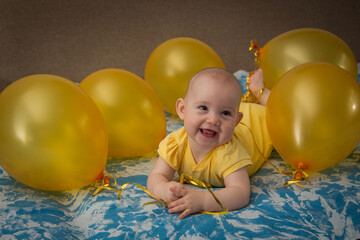 A small child in a yellow dress in the middle of yellow inflatable balloons