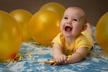 A small child in a yellow dress in the middle of yellow inflatable balloons