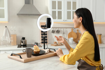 Blogger with tasty cake recording video in kitchen at home. Using ring lamp and smartphone