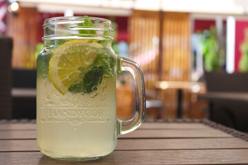Icy citrus lemonade in a jar with lemon, mint and ice on a wooden table on the terrace of cafe. Thirst quencher and detox concept. Selective focus
