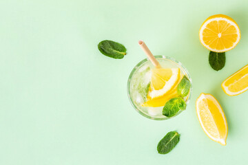 Ice lemon water or lemonade with mint on a green background. A glass of fresh fruit drink for summer heat. - obrazy, fototapety, plakaty