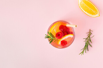 Lemon water or lemonade with raspberry and rosemary on a pink background, top view. Aromatic cool cocktail for the summer heat.