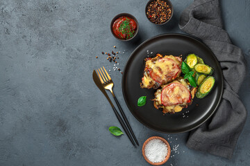 Baked meat with mushrooms, tomato and cheese on a dark gray background.