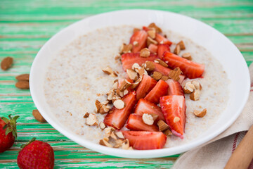 Oatmeal porridge with strawberries and almonds in a white plate on a rustic background