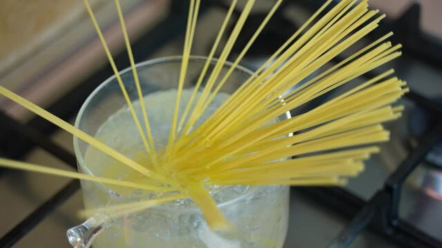 Overhead top view shot of a man's or cook's hand putting raw spaghetti into a pan full of boiling water to cook a healthy Italian dish of pasta macaroni.