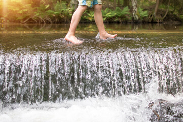 Kids legs walkingin watere  in stream in the summer. Outdoor, barefoot, holiday concept