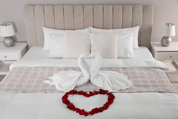 Beautiful composition on bed. Swans made of towels and rose petals arranged in heart shape