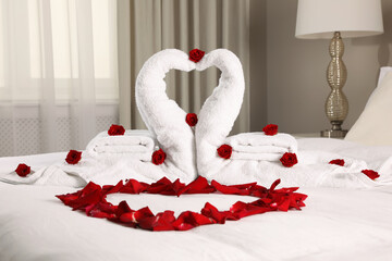 Beautiful composition on bed. Swans made of towels and rose petals arranged in heart shape