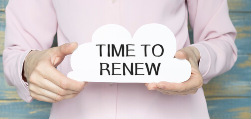 Woman writes in a notebook with a silver pen and hand holding card with text: TIME TO RENEW. Pink background, front view. Business and education concept.