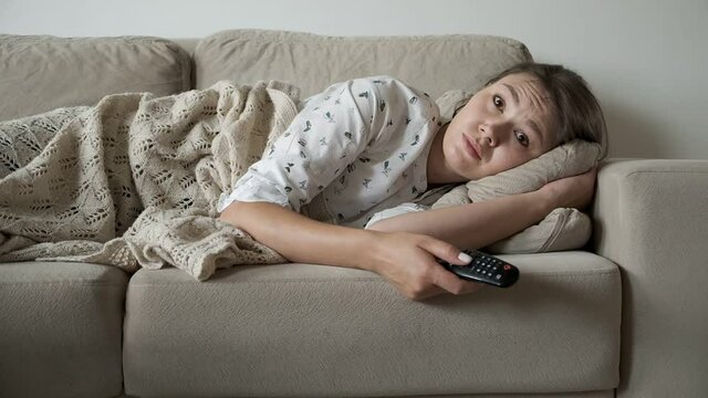 Bored woman watching tv lying on the couch, remote control switches channels