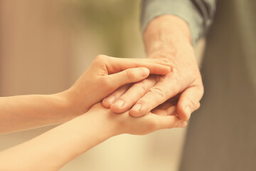 Helping hands on blurred background, closeup. Elderly care concept