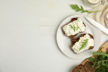 Bread with cream cheese and arugula on white wooden table, flat lay. Space for text