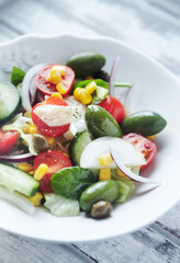 Healthy Salad with Green Olives, Baby Spinach, Cucumber, Cherry Tomatoes and Capers. Bright wooden background. Close up. 