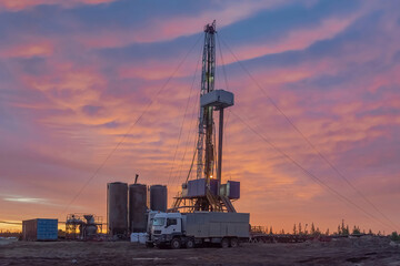 Fototapeta premium Drilling of deep well at the oil and gas field. In the foreground, cementing unit and cement bins. Compound cementing well. Beautiful northern sunset