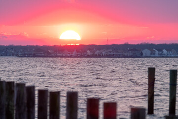 Vibrant sunset going behind a hill with houses on it, with a blurry fence in the foreground. Island...