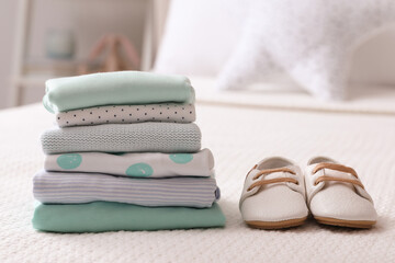 Stack of baby boy's clothes and shoes on bed at home, space for text