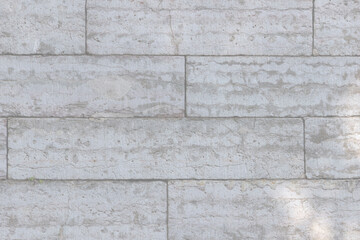 The texture of a gray stone wall made of rectangular marble blocks. Sunlight on the masonry.