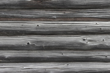 The wall of an old wooden house made of darkened weathered logs. Traditional Russian log hut.