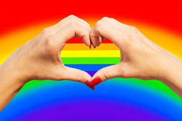 Gay pride concept. Womans hands making heart sign with gay pride LGBT rainbow flag
