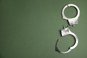 Classic chain handcuffs on dark green background, top view. Space for text