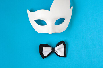 A black and white bow tie and a white carnival mask on a pastel blue background. Copy space.