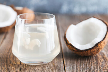 Coconut water in a glass close-up on a wooden table and a half of a fresh coconut lies nearby. Organic Coconut Detox Juice