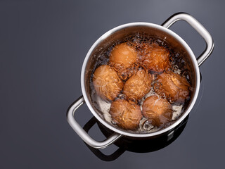 Chicken eggs are boiled in a saucepan on a glass ceramic induction hob. Cooking hard boiled eggs in a metal pan on electric stove. Brown shell eggs in a pot of hot water with bubbles.