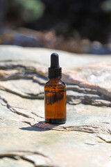 Skincare brown glass bottle container with dropper on natural stone. Photo with selective focus and harsh shadow