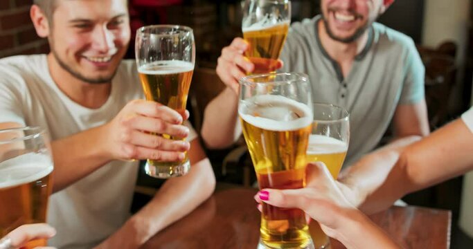 Smiling carefree friends enjoying drinking together in bar. Group of happy young men drinking cold draft beer, chatting and having good time at pub. Laughing men on night out drinking beer on counter.