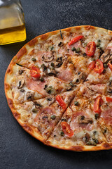 Pizza with tomatoes, ham, capers, mushrooms, mozzarella cheese, spices, sesame seeds and tomato sauce. On a dark background.