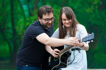 Brother teaching sister to play guitar in nature