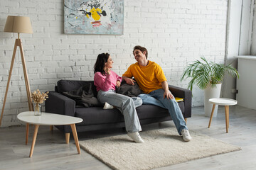 smiling young couple sitting on couch and looking at each other in modern living room
