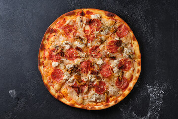 Pizza with sun-dried tomatoes, spicy sausage, chicken, onions, honey mushrooms, mozzarella cheese, spices and tomato sauce. Flat lay. On a dark background.