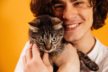 Cat in hands of blurred man smiling isolated on orange
