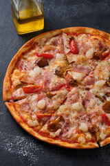 Pizza with tomatoes, bacon, pickled onions, honey mushrooms, mozzarella cheese, spices and tomato sauce. On a dark background.